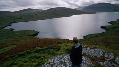 man contemplating a vast mountain lake landscape
