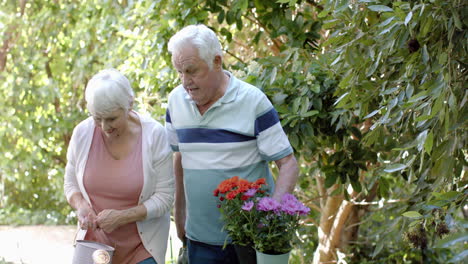 Pareja-Caucásica-Mayor-Sosteniendo-Flores-En-Un-Jardín-Soleado,-Cámara-Lenta