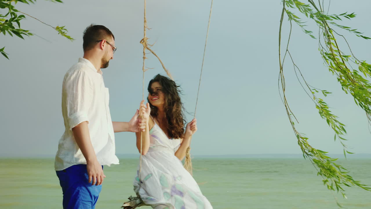 한 청년이 빗속에서 바다를 배경으로 그네를 타고 소녀를 굴리고 있다.