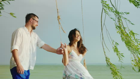 A-Young-Man-Is-Rolling-His-Girl-On-A-Swing-Against-The-Background-Of-The-Sea-In-The-Rain-Romance-And