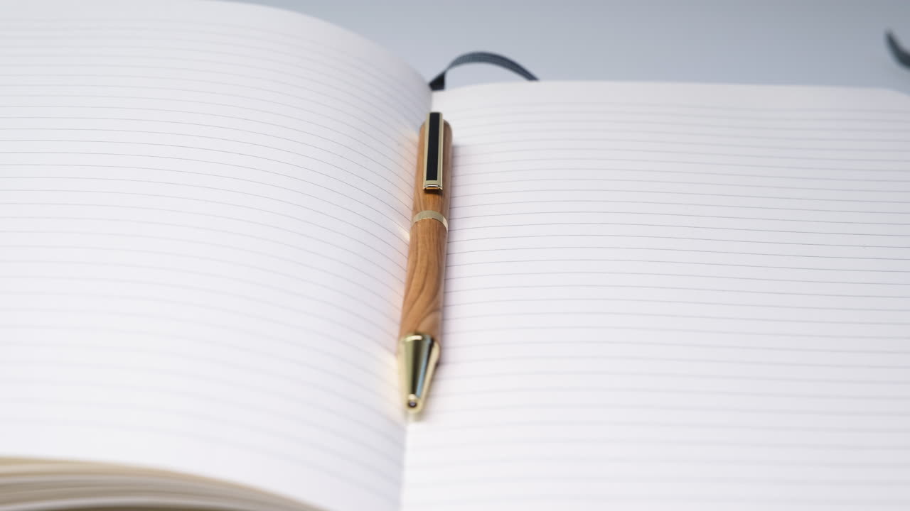 Close up shot of a pen resting on a blank notebook placed on a white table creating a simple and minimal writing concept