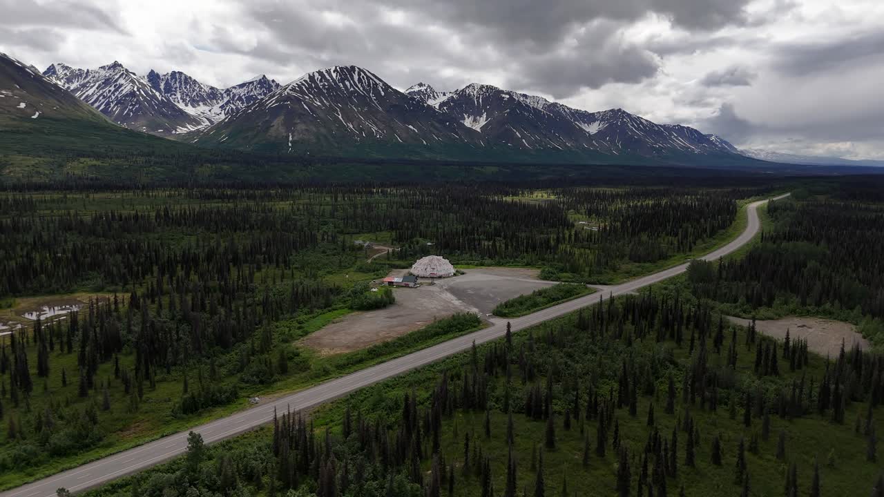 Drone Slowly Panning around abandoned Rest Stop surrounded by trees along Parks Highway in Cantwell Alaska, Talkeetna Mountains and Cloudy Sky