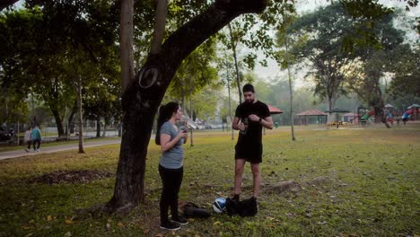 couple hydrating and resting during an outdoor workout in a park