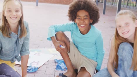 Video-portrait-of-happy-diverse-schoolchildren-making-protest-placards-in-schoolyard,-copy-space