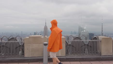 new york usa. a man in rainy jacket walking on top of the rock observation deck with view of manhattan under clouds