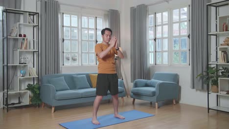 hombre asiático haciendo yoga en meditación sukhasana de pie en la alfombra en casa