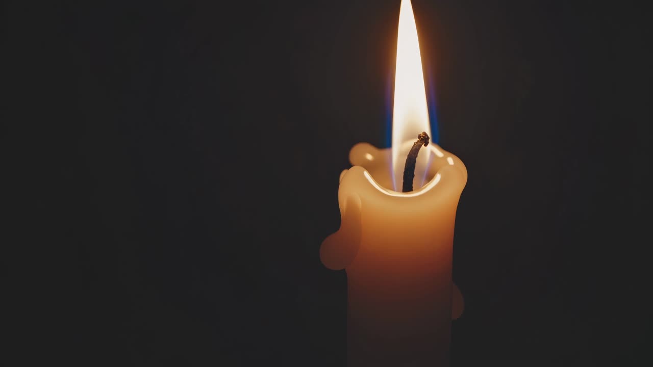 Detailní video plamene svíčky na tmavém pozadí, záběr z bočního úhlu.