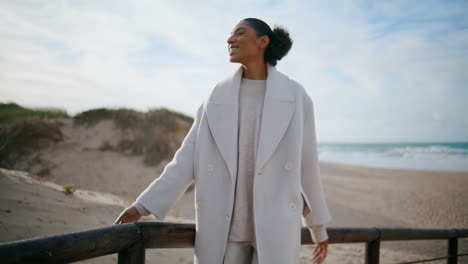 Happy-woman-lean-railings-at-sand-beach-dunes.-Cheerful-african-american-admire