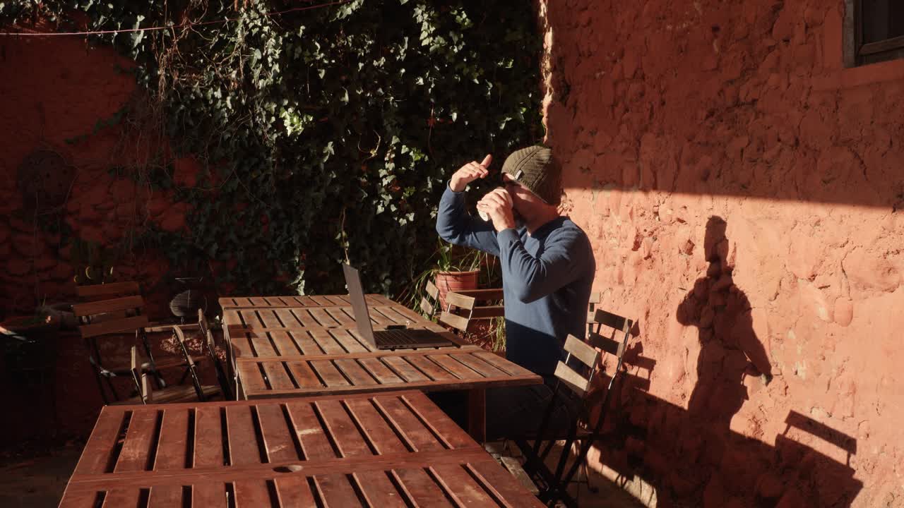 A man working outside a rural house with his laptop, making a pause and drinking coffee