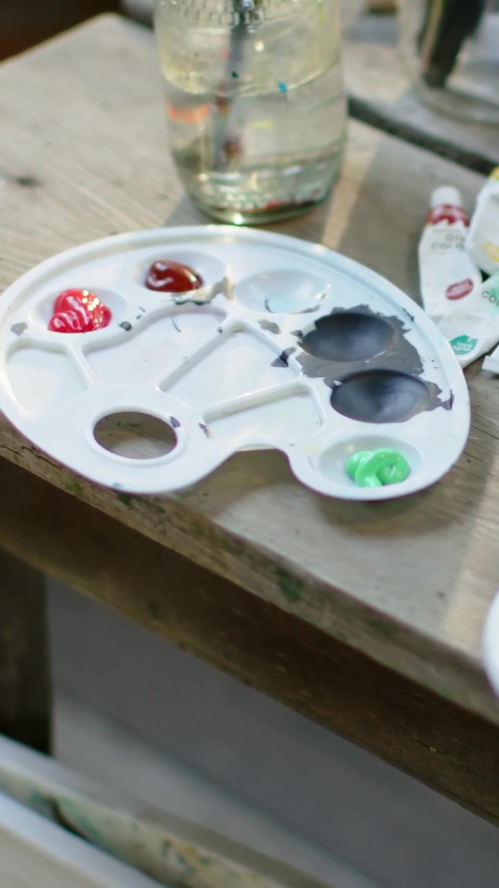 Vertical video: Panning camera moving right to center palette on wooden bench, with jar, paint tube