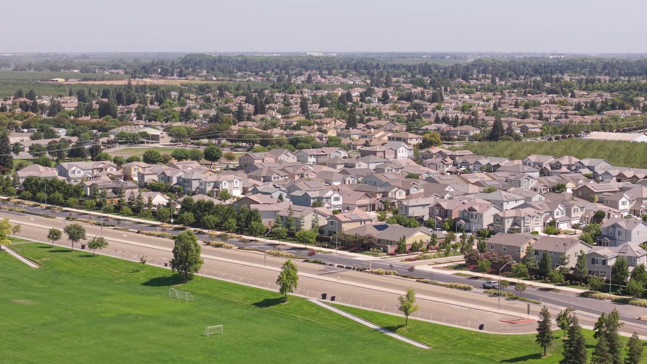 Drone receding from road toward soccer fields with residential view.