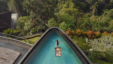 aerial view woman having breakfast in swimming pool enjoying exotic food at luxury hotel spa with view of tropical jungle