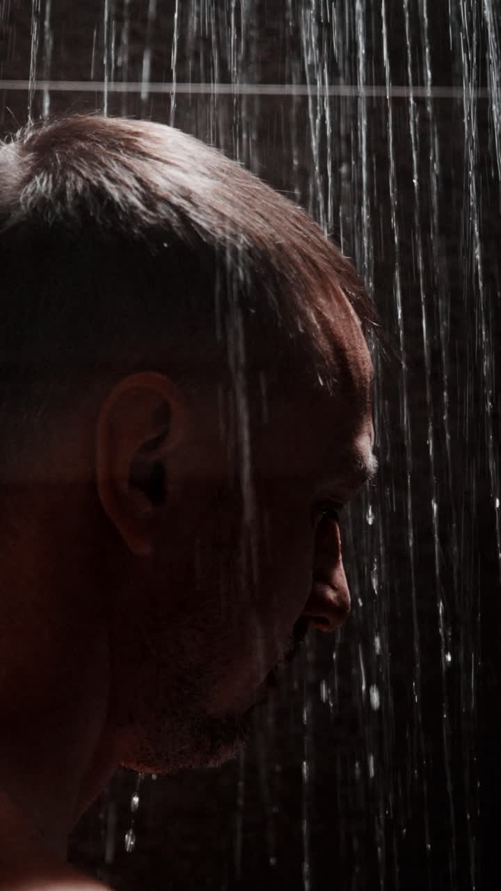Man experiencing a refreshing shower under cascading water in a dimly lit space