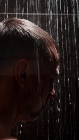 man experiencing a refreshing shower under cascading water in a dimly lit space