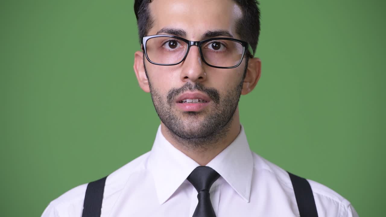 Young handsome bearded Persian businessman against green background