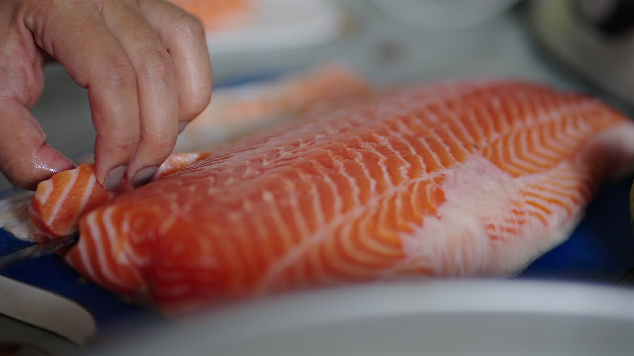 Person's Hand Slicing Meat Of Salmon. - closeup shot