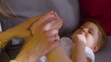 Close-Up-View-Of-A-Baby-Lying-On-The-Sofa-At-Home-While-His-Mother-Playing-With-Him-And-Holding-His-Legs