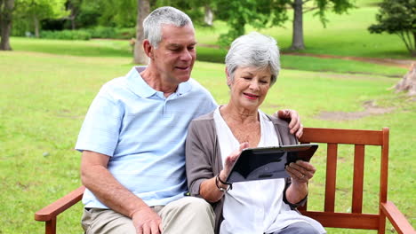 retired couple sitting on a park bench using a tablet