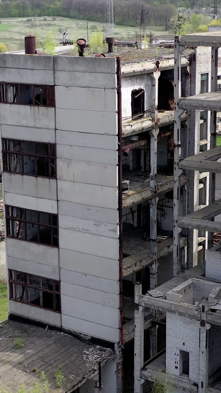 Damaged industry. Abandoned place with old unfinished buildings of a factory. Old industrial plant in springtime. Drone view. Vertical video
