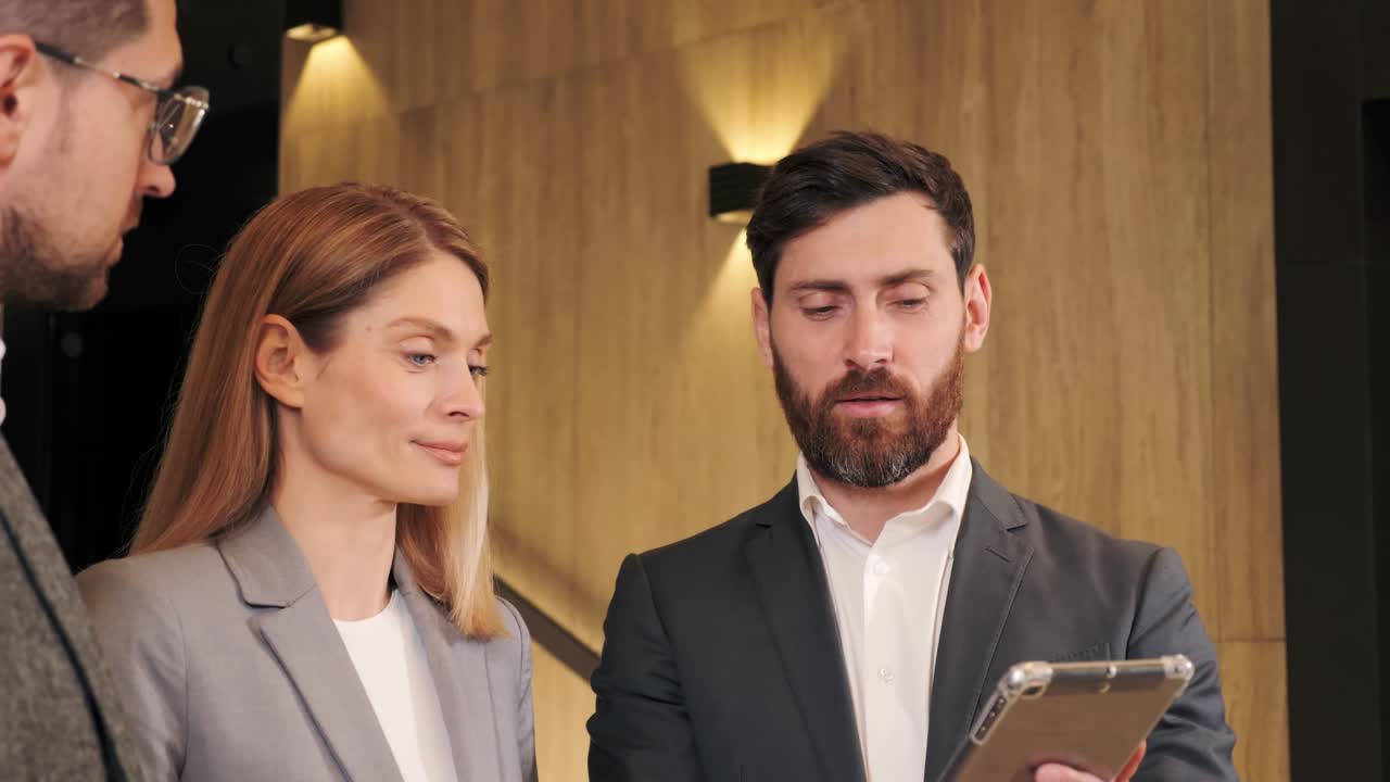 бизнесмен показывает проект на планшетном компьютере. исполнительная команда бизнесмены слушают генерального директора, ведут переговоры, обсуждают результаты в коридоре. стильные руководители компании, менеджер, консультант, разговаривающий в помещении.