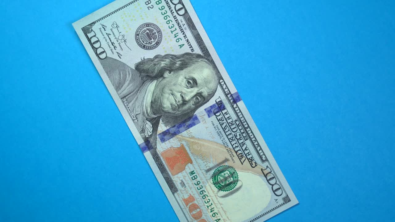 Cento dollari che ruotano lentamente su uno sfondo blu rotante