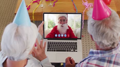 Kaukasisches-älteres-Paar-Mit-Partyhüten-Auf-Laptop-Videochat-Während-Weihnachten-Zu-Hause