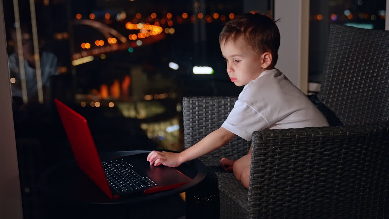 Curious toddler plays with a laptop. Little kid watches cartoons or plays games in the evening