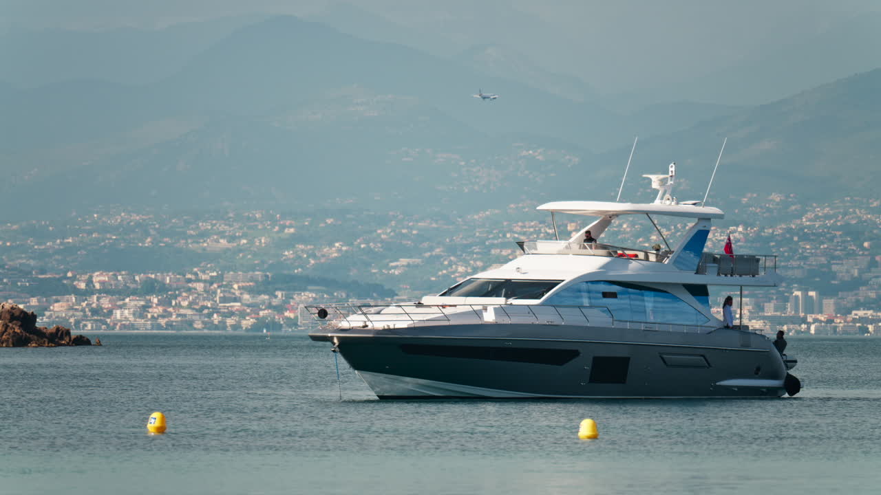 Antibes, France - May 6, 2025: People on a boat docked on the sea with the city and mountains on the background in daylight