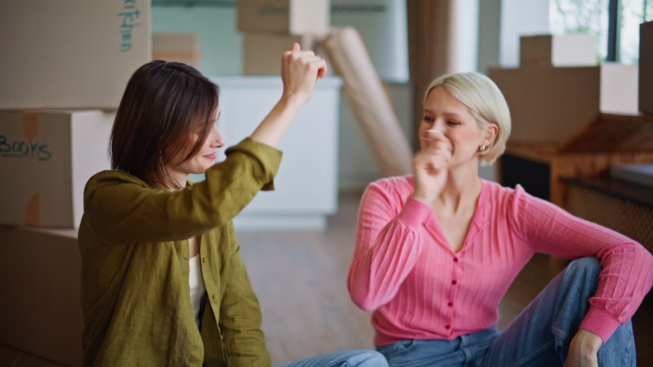 Amiche stanche che si trasferiscono, sedute in salotto, che ridono tra scatole di cartone