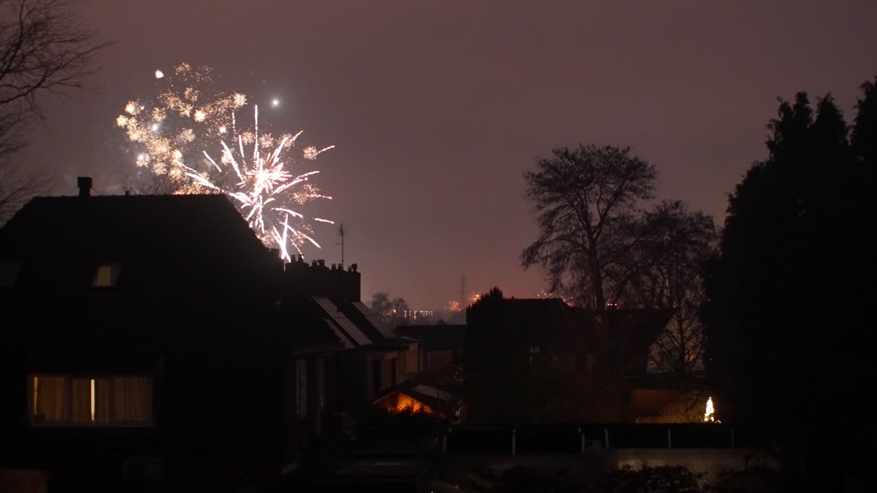 Rood vuurwerk dat in de nachtelijke hemel ontploft boven huizen in een buitenwijk van Oosterbeek tijdens nieuwjaar