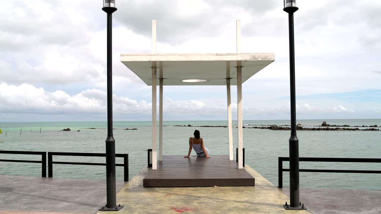 A woman sits on a pier and looking at the sea