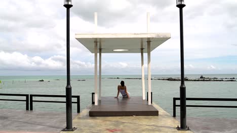 una mujer se sienta en un muelle y mira al mar