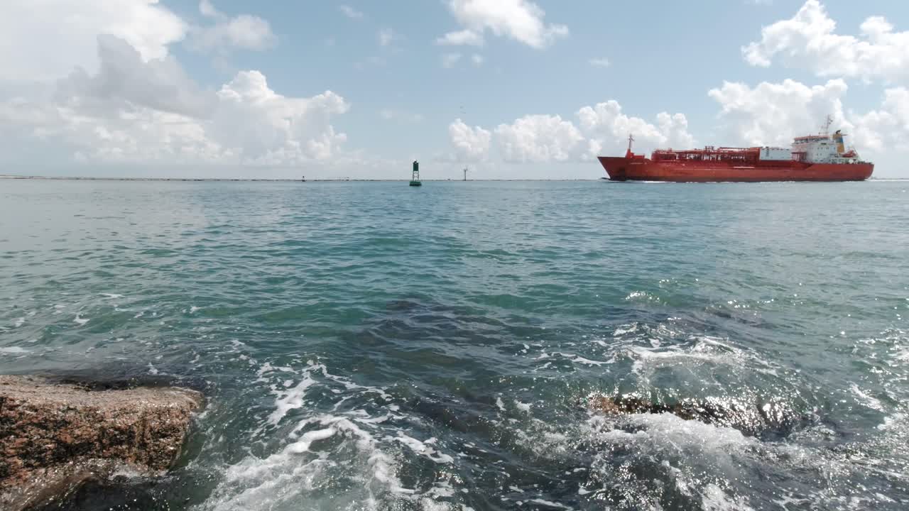 파도가 멕시코만에 있는 텍사스 주 포트 아란사스의 화강암 바위에 부딪히면서 산업용 선박이 방파제 사이의 수로에 떠 있습니다.