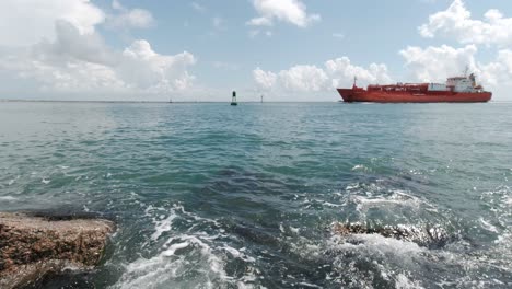 Un-Barco-Industrial-Flota-En-El-Canal-Entre-Los-Embarcaderos-Mientras-Las-Olas-Golpean-Las-Rocas-De-Granito-En-Port-Aransas,-Texas,-En-El-Golfo-De-México