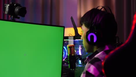 close up back view of asian boy streamer screaming goal celebrating winning game on green screen computer. live stream on desk illuminated by rgb led strip light