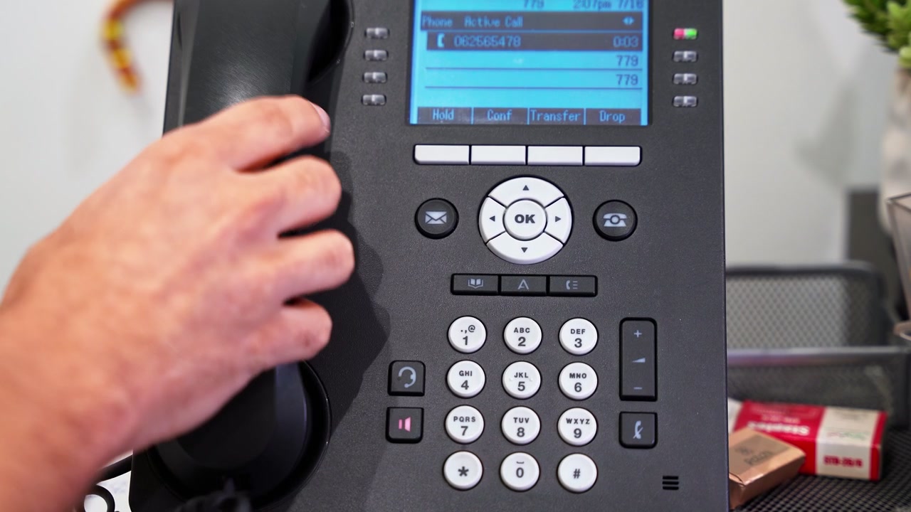 Close-up of a hand pressing buttons to dial a phone number on a modern black office desk phone in a professional workspace, illustrating corporate communication and business operations.