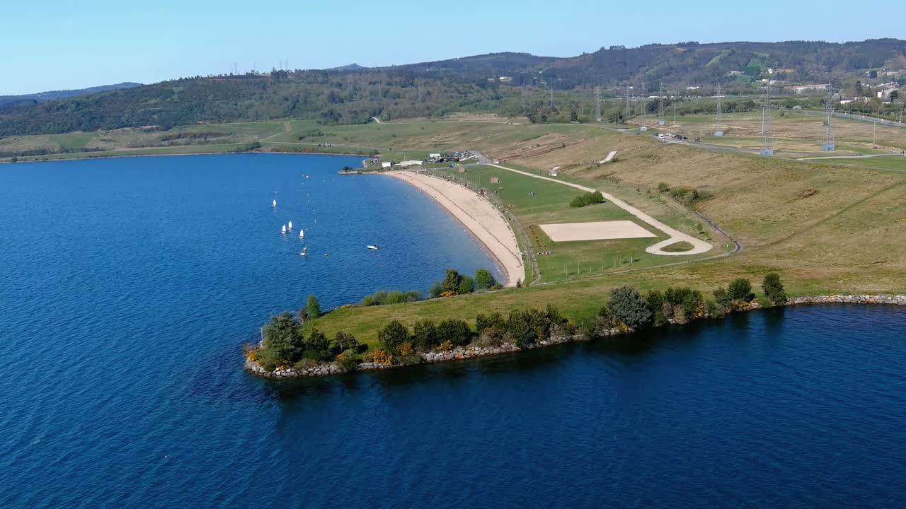 gran lago con jardín para pasear, playa y zona para tomar el sol con césped donde se imparten clases de vela, día soleado
