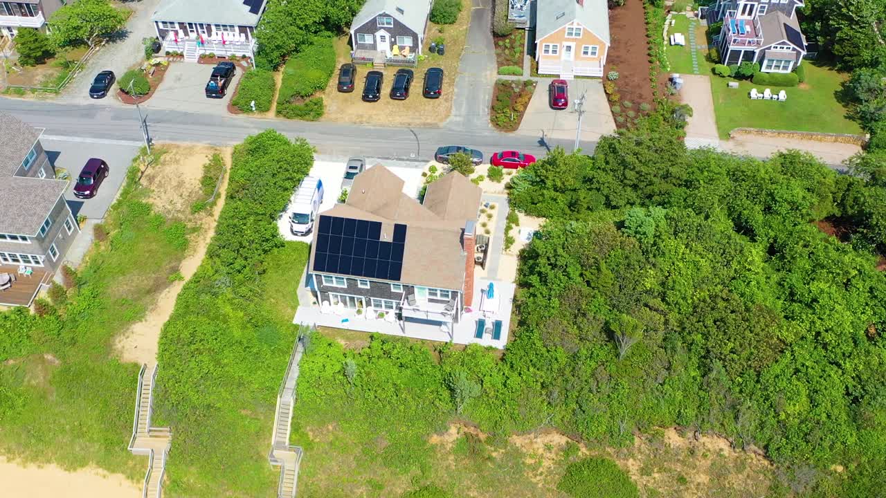 Cape Cod shoreline home sits framed by greenery, sandy beach stretching outward, and turquoise ocean glimmering in soft afternoon light across the coast