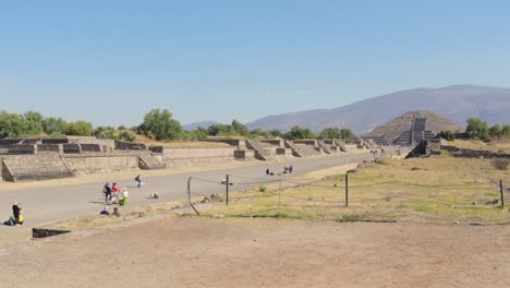 a wide dolly in shot of the archaeological site of teotihuacan in mexico, with the pyramid of the moon in the background and some tourists around, on a clear and sunny day