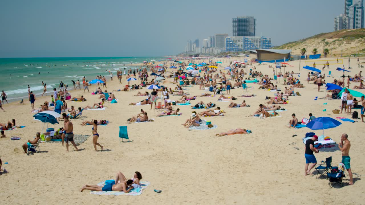 Time lapse view of the Beach showing relaxing tanning people on sand with towels and colourful umbrellas. Timelapse footage of enjoying crowed at the beach on a summer day.