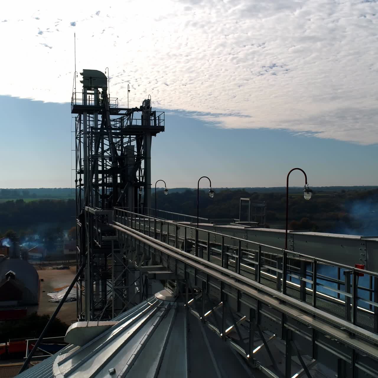 Top of industrial plant. Modern elevators and metal tower on nature background. Smoke goes from large factory in the countryside. Aerial view.