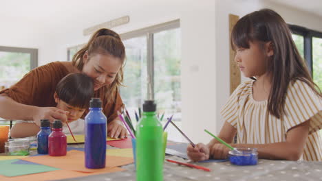 madre asiática divirtiéndose con los niños haciendo artesanía en la mesa en casa