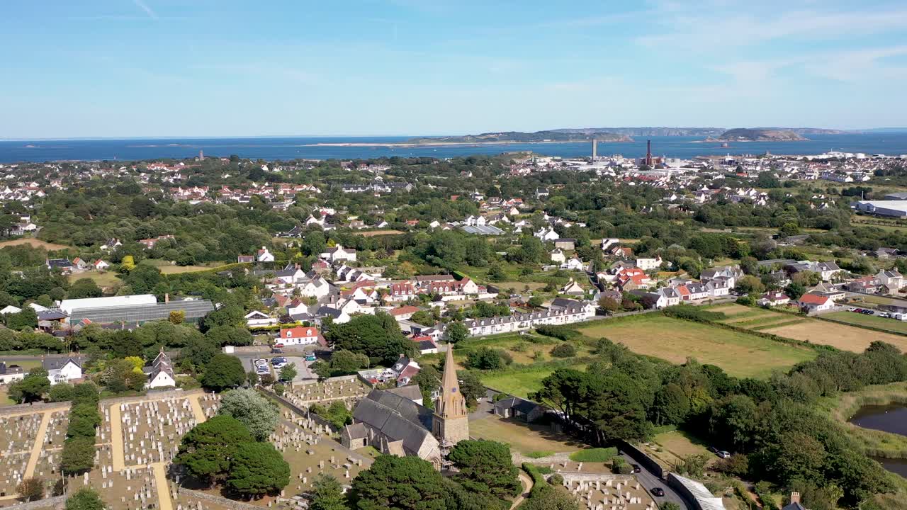imágenes de drones sobre la iglesia de vale y el cementerio en el norte de guernsey con vistas a herm, jethou y sark que muestran campos, casas, st sampson, la costa noreste y la central eléctrica