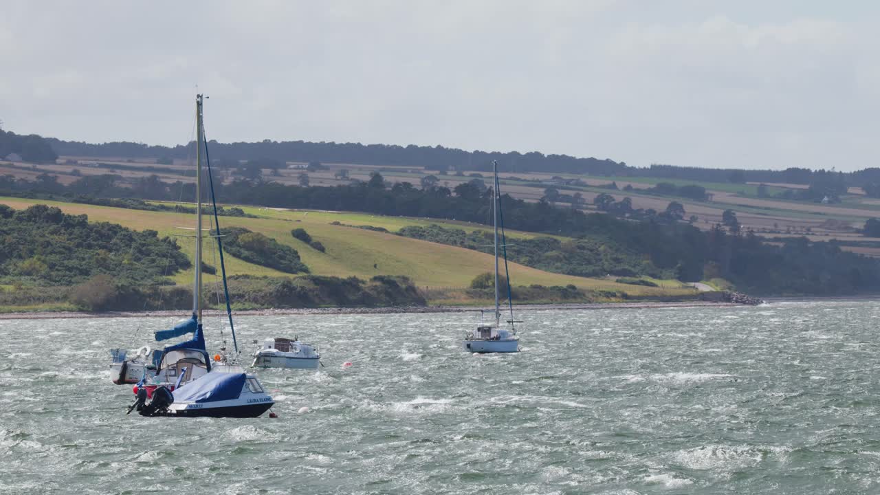 Multiple sailboats move on choppy coastal waters, overcast skies, steady camera, scenic Scottish hills