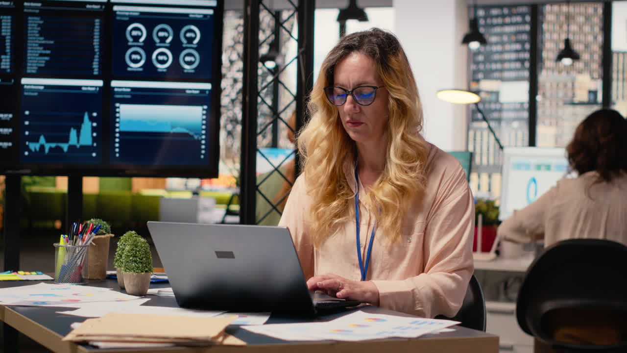 Video verticale: Donna d'affari alla sua scrivania che analizza dati visualizzati sul suo laptop