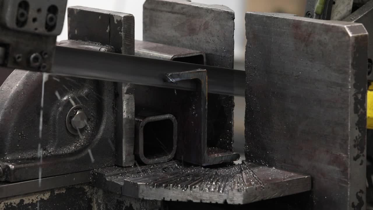 Sega a nastro automatica in funzione, che taglia un albero metallico con liquido refrigerante.