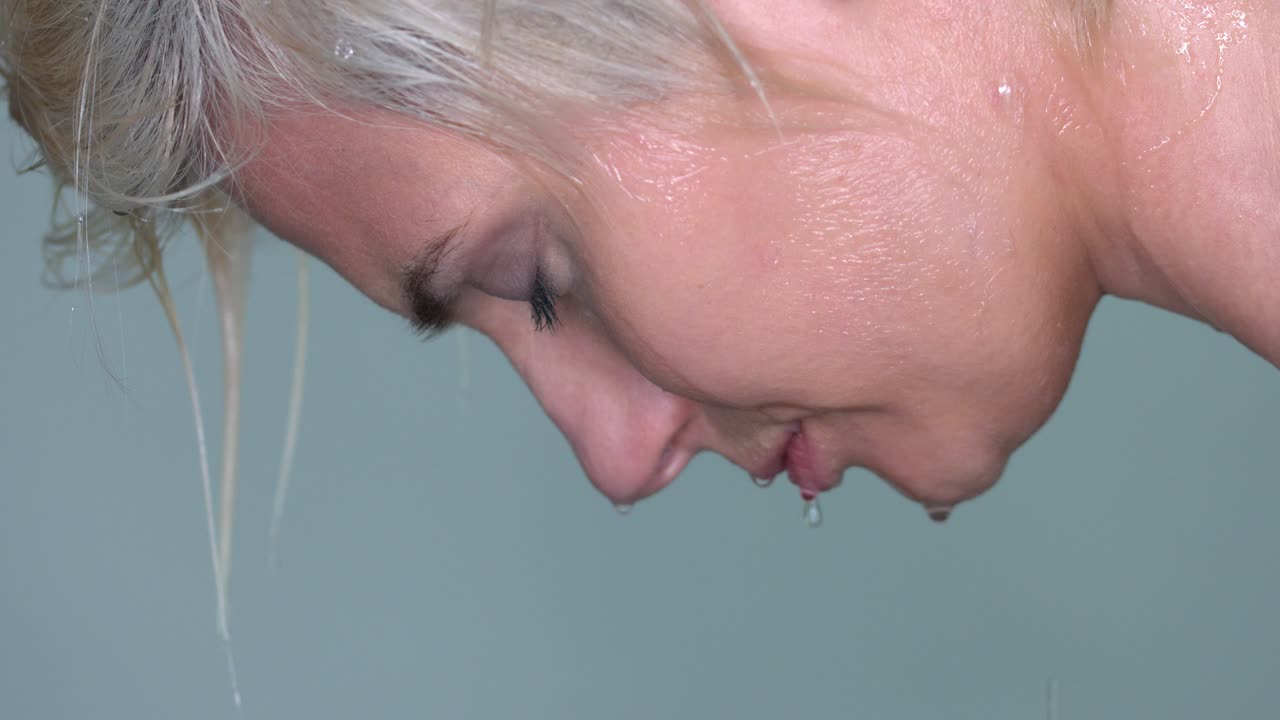매끄러운 회색 스튜디오 배경에서 물이 떨어지는 여성의 얼굴 클로즈업