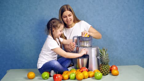 happy mother and daughter squeezing fruits for juice. beautiful woman is holding orange and making juice. little girl helps her mother in the kitchen. fresh fruit.