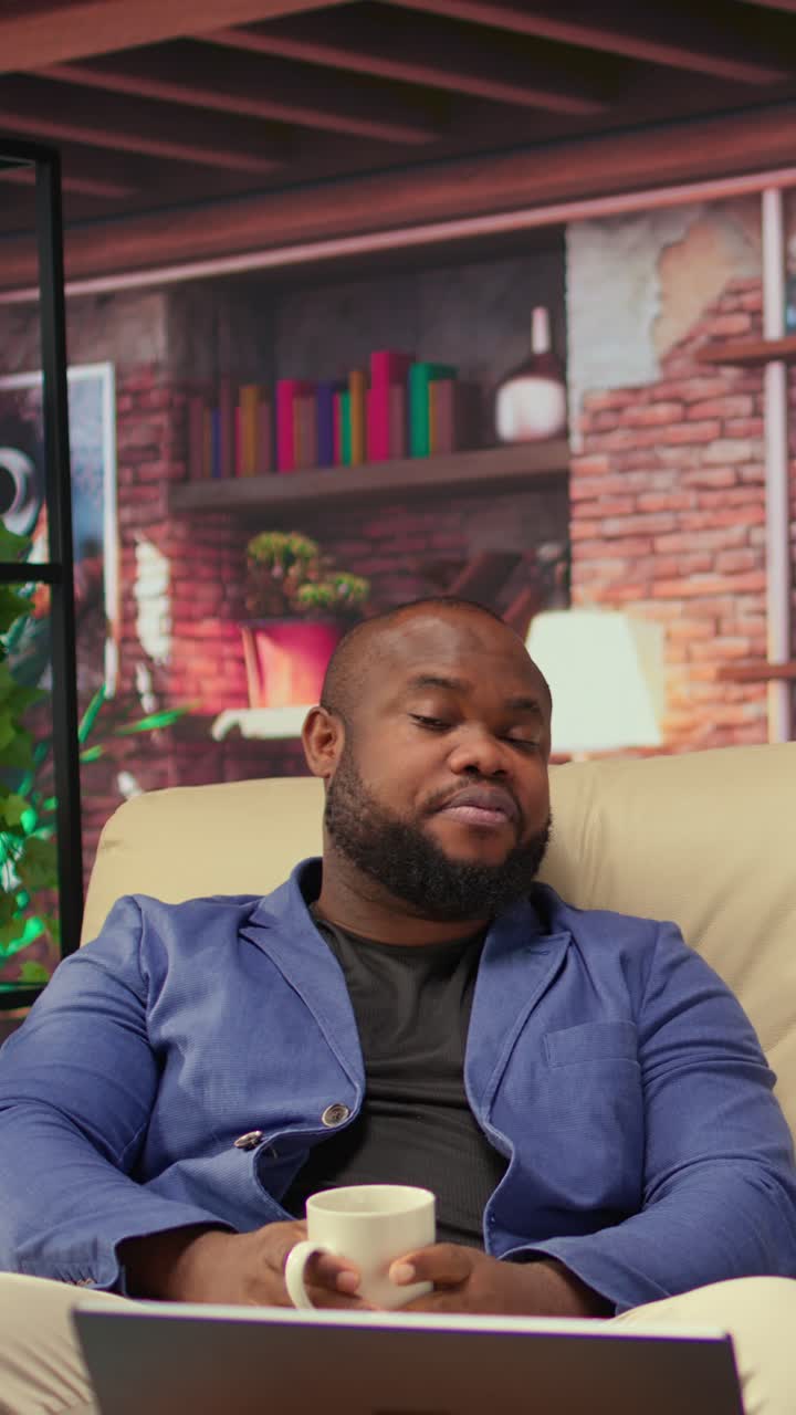 Glad afroamerikansk mann snakker og ler på sofaen