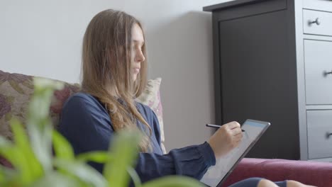 Caucasian-teenage-girl-with-serious-expression-using-tablet-on-sofa-at-home